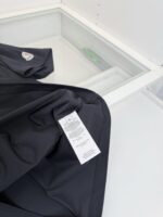 Dettaglio di abbigliamento nero con etichetta di cura e sfondo moderno e luminoso.