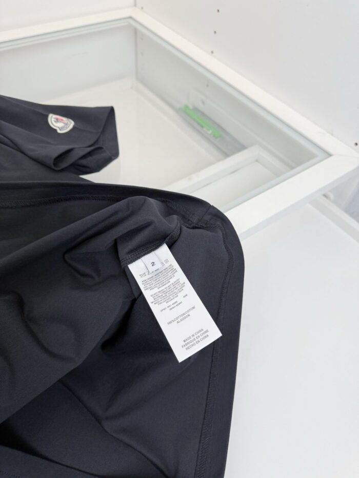 Dettaglio di abbigliamento nero con etichetta di cura e sfondo moderno e luminoso.