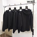 Magliette con cappuccio nere in esposizione con la scritta wait per lattenzione.