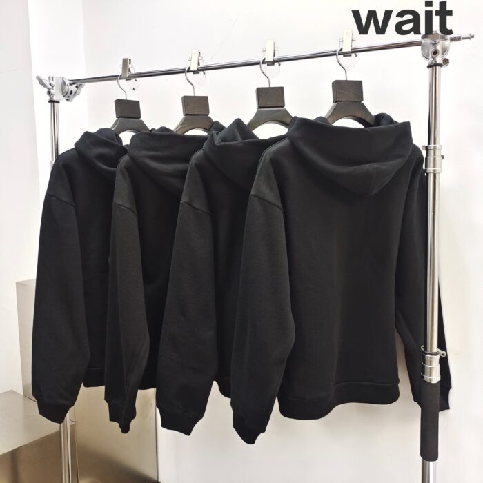 Felpe nere in vetrina con testo wait, stile minimalista e atmosfera di attesa.