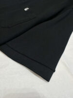 Maglia nera con logo sottile, finiture accurate e tessuto morbido, sfondo chiaro.