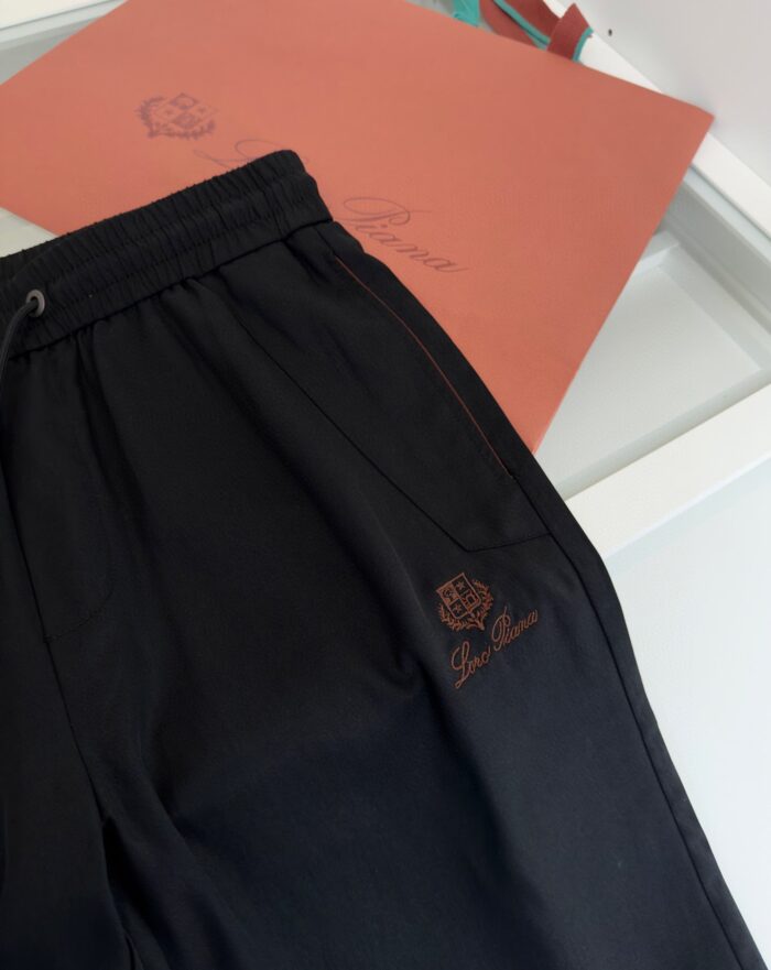 Pantaloni jogger neri con logo marrone e packaging corallo, stile sportivo di alta qualità.