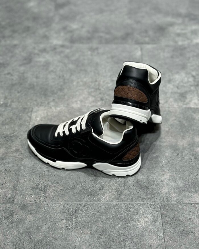 Sneakers high-top in pelle nera con dettagli marroni, suola antiscivolo e stile urbano moderno.