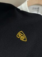 Maglietta nera con logo ricamato giallo e dettagli di stile elegante e moderno.