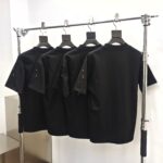 Magliette nere minimaliste su supporto industriale, stile moderno, dettagli curati, perfette per ogni occasione.