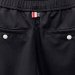 Pantaloni neri sportivi con tasche, bottoni bianchi e dettaglio emblematico colorato.