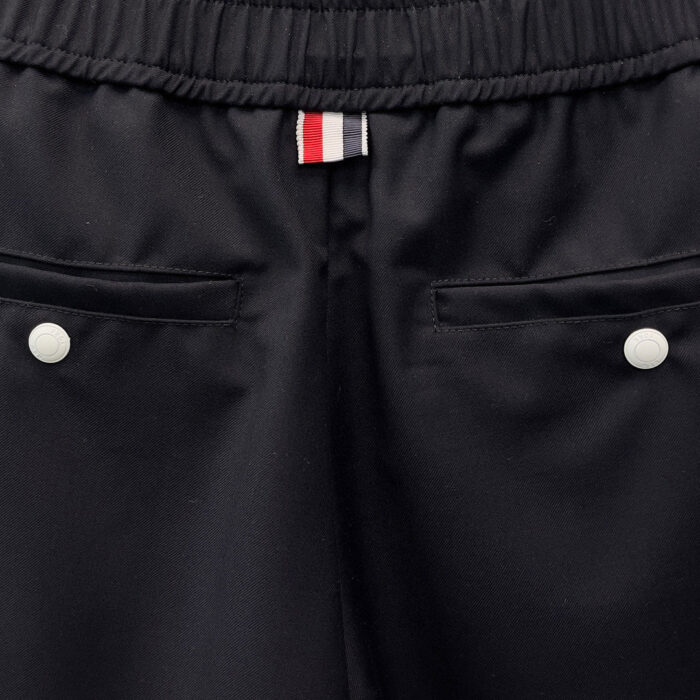 Pantaloni neri sportivi con tasche, bottoni bianchi e dettaglio emblematico colorato.