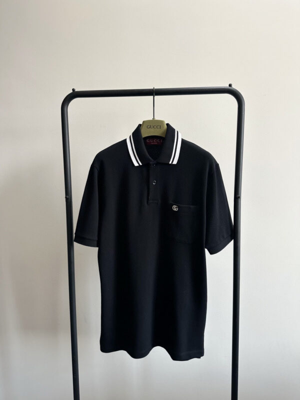 Polo nera minimalista con dettagli a strisce, tasca e stile elegante su appendiabiti moderno.