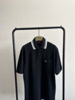 Maglietta polo nera minimalista con colletto a righe su appendiabiti moderno.