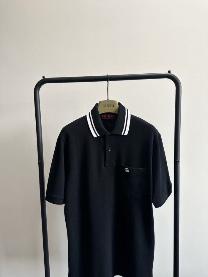 Maglietta polo nera minimalista con colletto a righe su appendiabiti moderno.