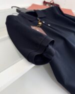 Maglietta polo nera elegante con manica rollata su superficie riflettente.