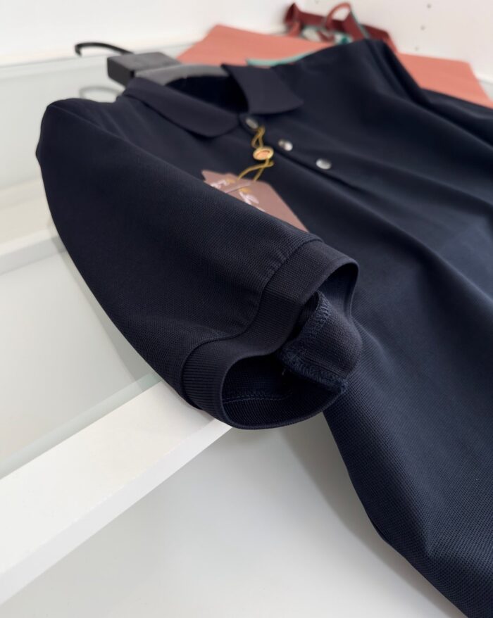 Maglietta polo nera elegante con manica rollata su superficie riflettente.