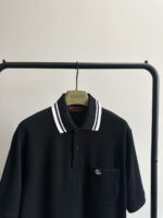 Polo nera Gucci con colletto a righe, elegante e versatile, su appendiabiti in metallo nero.