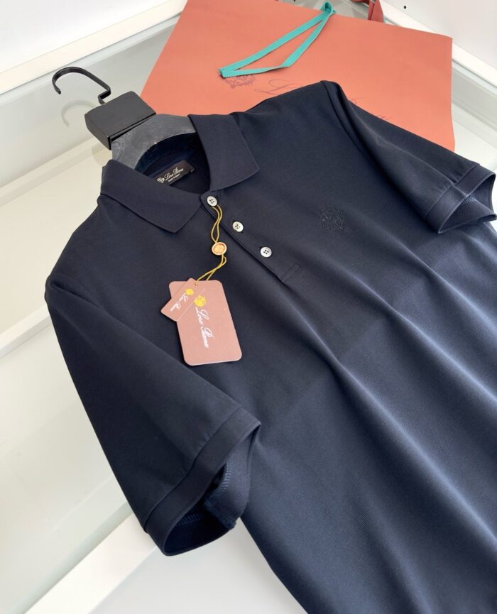 Maglietta polo nera con etichetta rosa, sfondo con shopping bag colorato e stile moderno.