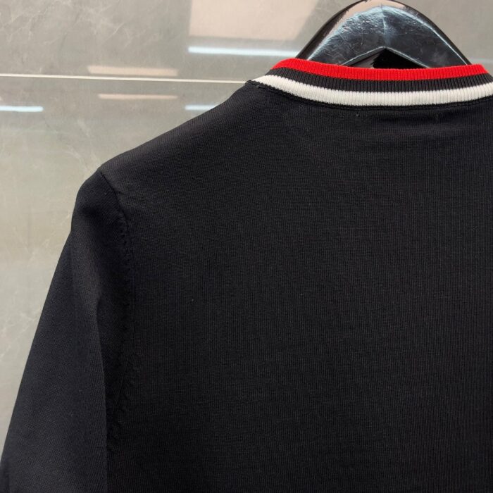 Maglietta polo nera con colletto a strisce rosse e bianche, stile sportivo e casual elegante.