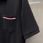 Maglietta polo nera con tasca a righe colorate e maniche arrotolate, stile casual elegante.