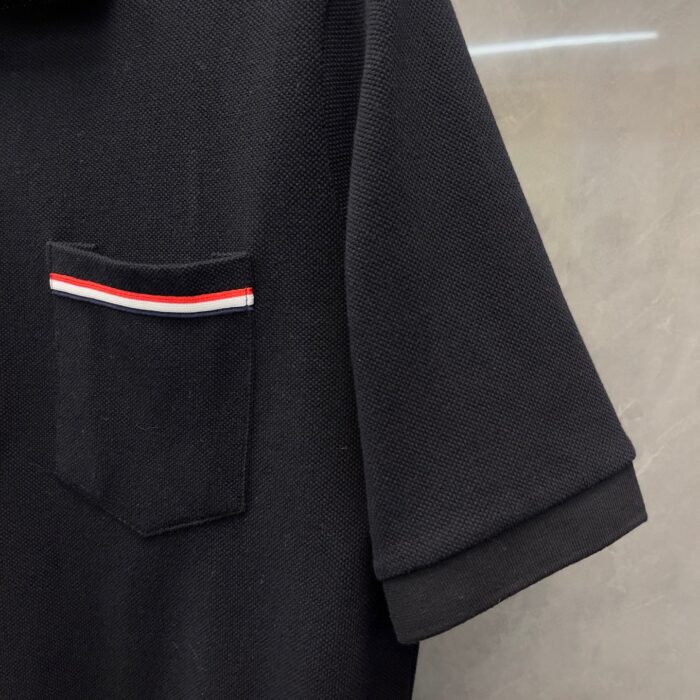 Maglietta polo nera con tasca a righe colorate e maniche arrotolate, stile casual elegante.