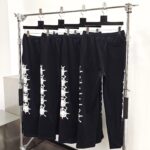 Pantaloni neri con ricami di teschi e ossa, stile urban edgy, su supporto industriale.