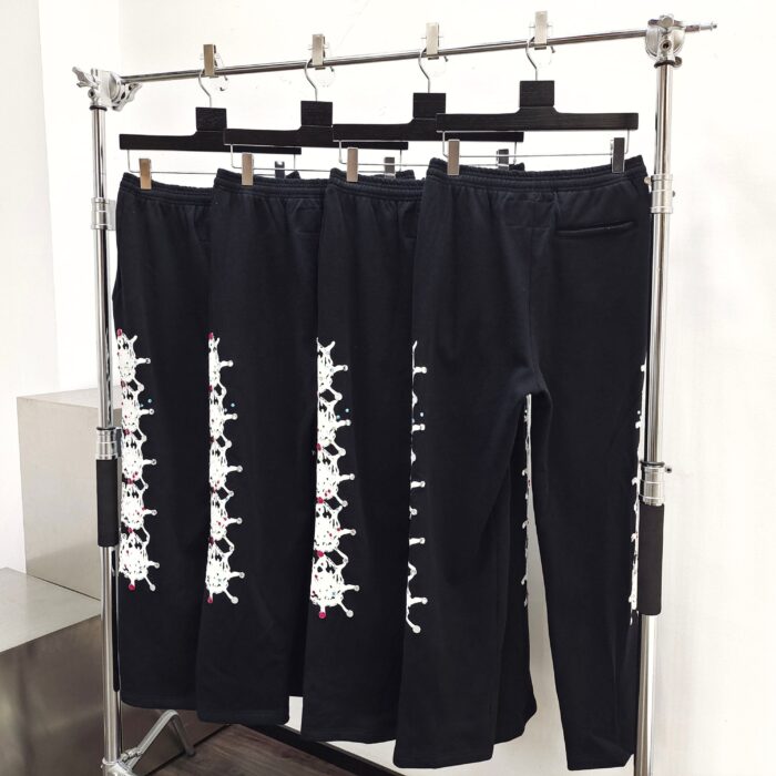 Pantaloni neri con ricami di teschi e ossa, stile urban edgy, su supporto industriale.