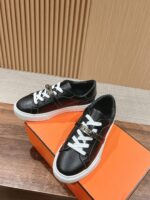 Sneakers nere eleganti con dettagli metallici su scatola arancione, stile moderno e sofisticato.