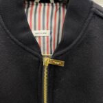 Giaccone nero con zip dorato, interno a righe e originato in Giappone, stile elegante e caldo.