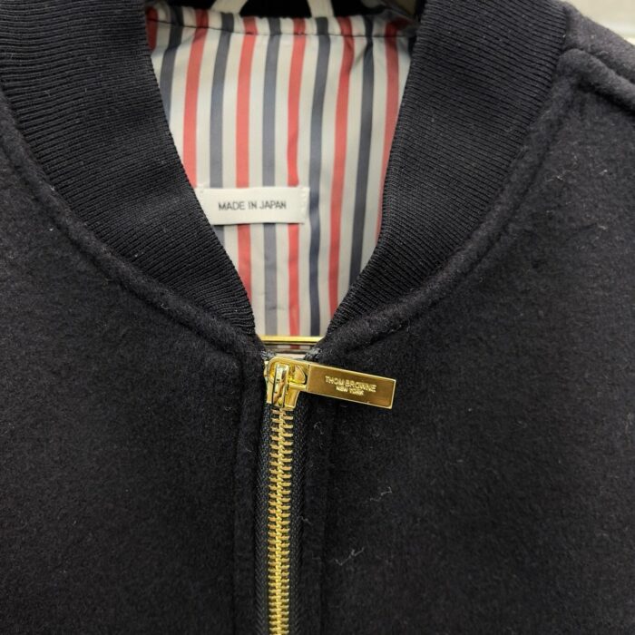 Giaccone nero con zip dorato, interno a righe e originato in Giappone, stile elegante e caldo.