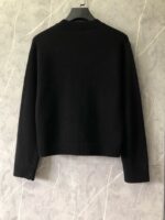 Maglione nero classico su gancio, stile minimalista, sfondo in marmo grigio elegante.