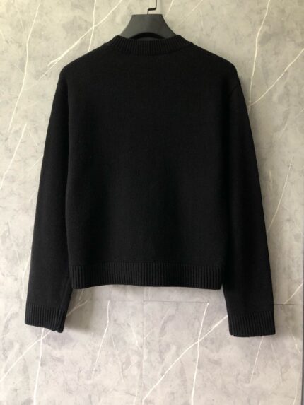 Maglione nero classico su gancio, stile minimalista, sfondo in marmo grigio elegante.