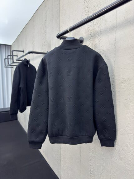 Maglione nero minimalista appeso in setting moderno con parete di cemento e luce soffusa.