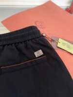 Pantaloni neri elasticati con tasca rossa, etichetta di qualità, sfondo salmone elegante.