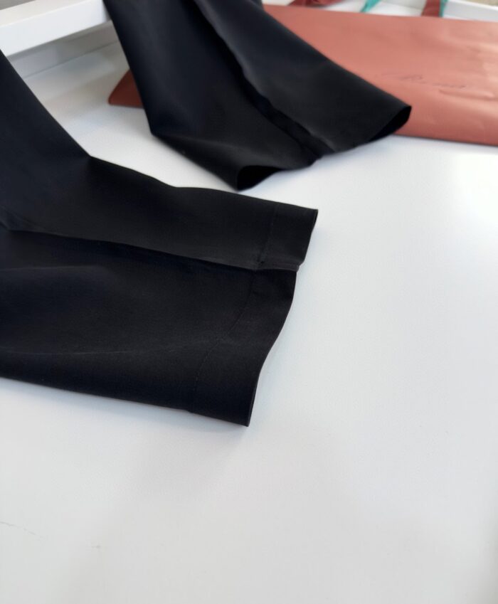 Pantaloni neri eleganti con borsa rust colorata, stile sofisticato su tavolo bianco.