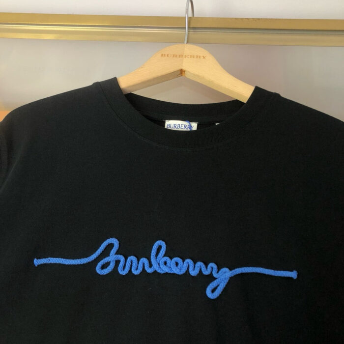 T-shirt nero con ricamo blu Burberry su appendiabiti in legno.