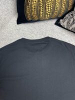 Maglietta nera minimalista su divano con cuscini colorati, atmosfera calda e rilassante.