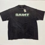 Maglietta nera oversize con logo SAINT effetto gradient verde e bianco, stile streetwear casual.