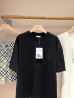 Maglietta nera ricamata, camicia chiara e capo quadri su appendiabiti in negozio elegante