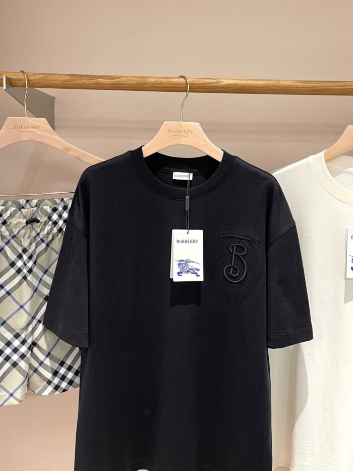 Maglietta nera ricamata, camicia chiara e capo quadri su appendiabiti in negozio elegante