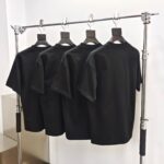 Rastrelliera industriale con quattro magliette nere in stile moderno, ambiente minimalista e luminoso.
