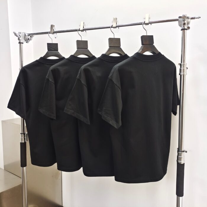Rastrelliera industriale con quattro magliette nere in stile moderno, ambiente minimalista e luminoso.