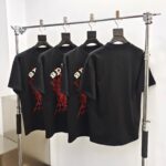 T-shirt neri con web di ragno rosso, stile streetwear, in esposizione moderna e minimalista.
