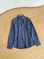 Camicia blu navy a maniche lunghe su pavimento in legno, stile elegante e curato.
