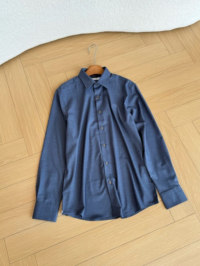 Camicia blu navy a maniche lunghe su pavimento in legno, stile elegante e curato.