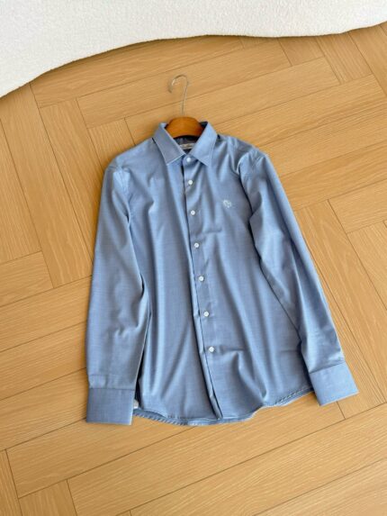Camicia azzurro chiaro maniche lunghe su pavimento in legno, stile elegante e casual.