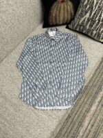 Camicia navy con motivo geometrico, maniche leggermente arrotolate, su sofa elegante con cuscino decorativo.