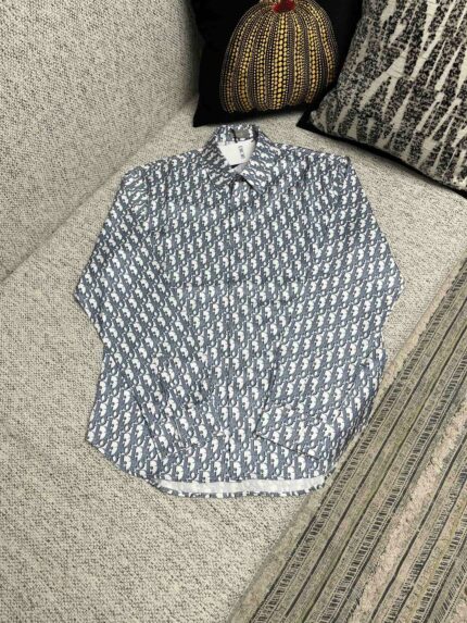 Camicia navy con motivo geometrico, maniche leggermente arrotolate, su sofa elegante con cuscino decorativo.