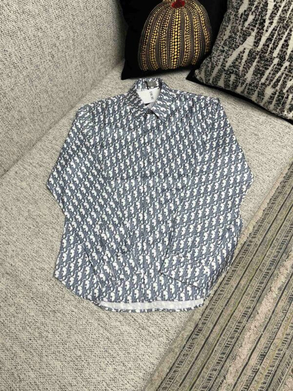 Camicia navy con motivo geometrico, maniche leggermente arrotolate, su sofa elegante con cuscino decorativo.