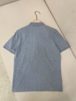 Maglietta polo blu minimalista su appendiabiti di legno, stile semplice ed elegante, perfetta per ogni occasione.