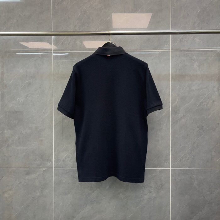 Maglietta polo blu scuro su stendino in ambiente minimalista con pareti grigie.