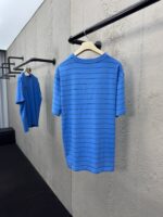 Magliette a righe blu casual e moderne su gruccia in ambiente minimalista.