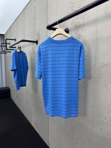 Magliette a righe blu casual e moderne su gruccia in ambiente minimalista.