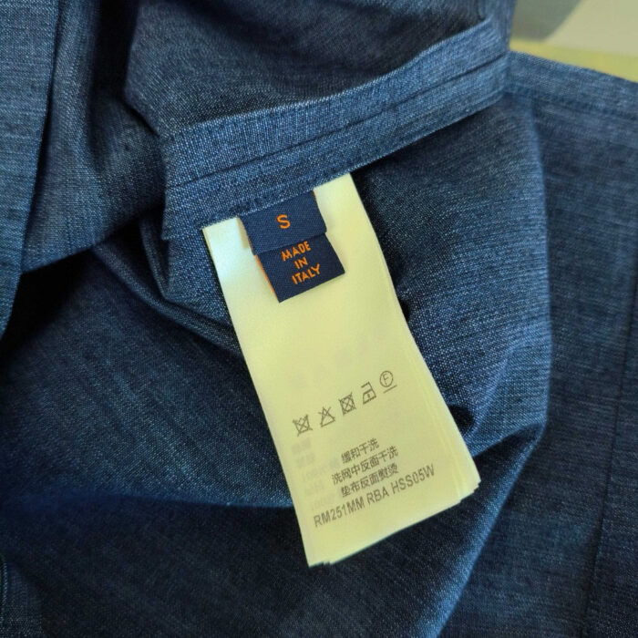 Etichetta di maglietta blu con logo, tag S e istruzioni di cura plurilingue.